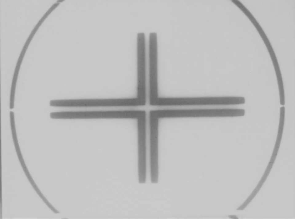 A black and white film frame with technical markings, a cross in the center of a circle.