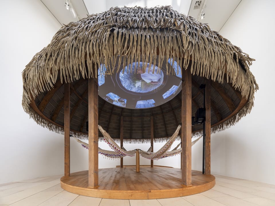 An African hut placed inside of an art gallery, with video images projected onto the roof.